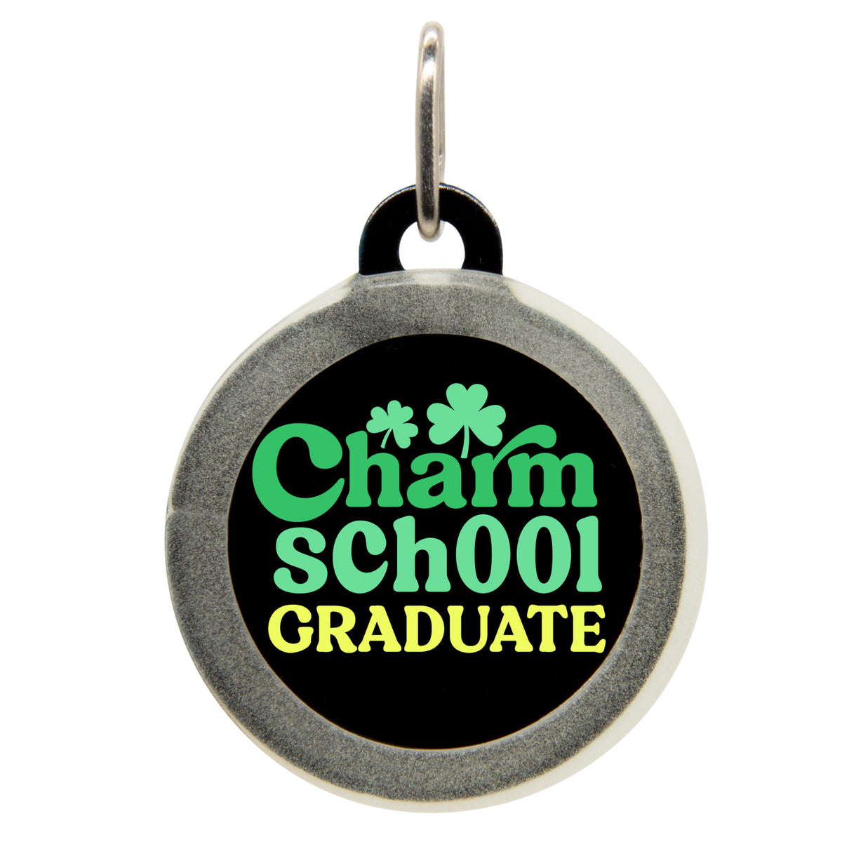 A black pet ID tag with the text &quot;Charm sch00l GRADUATE&quot; in green and yellow, featuring shamrocks. The tag has a small metal loop at the top for attaching to a collar.