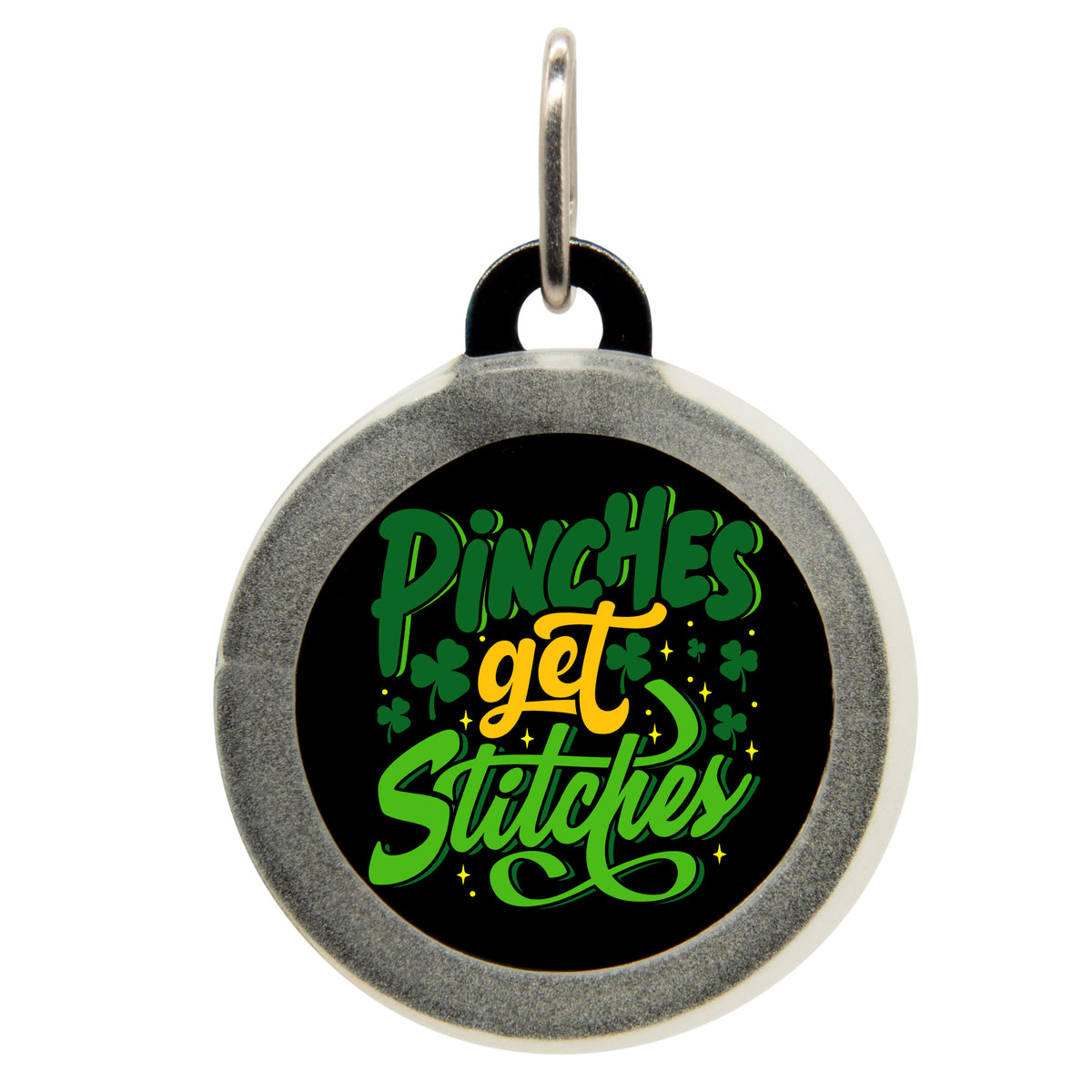 A black pet ID tag with the text &quot;Pinches get Stitches&quot; in green and yellow, surrounded by shamrocks and stars. The tag has a small metal loop at the top for attaching to a collar.